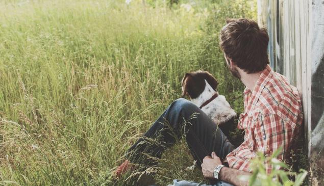 A man and a dog are sitting on grass